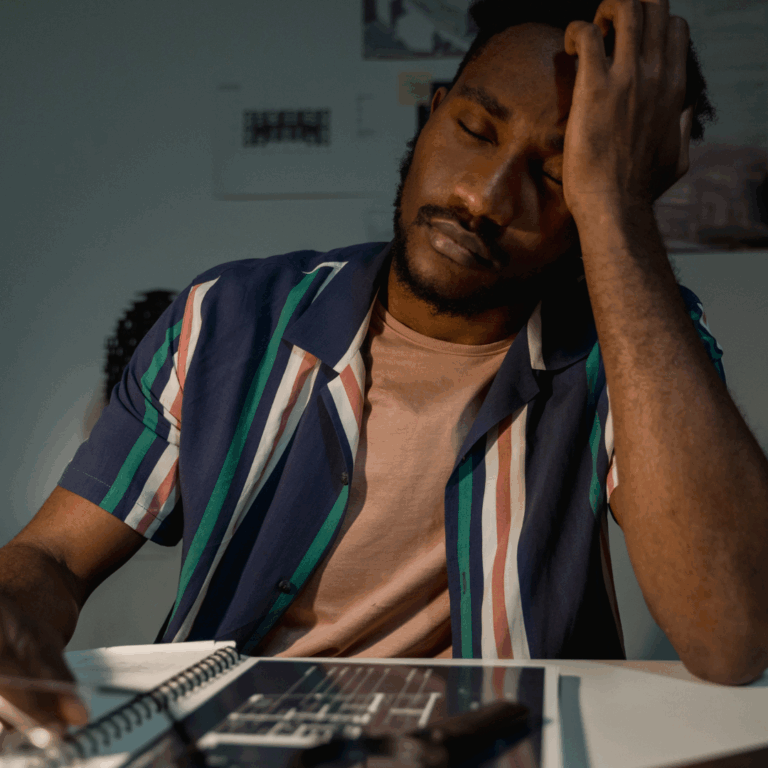 man sitting at table, eyes closed, resting his head on his hand