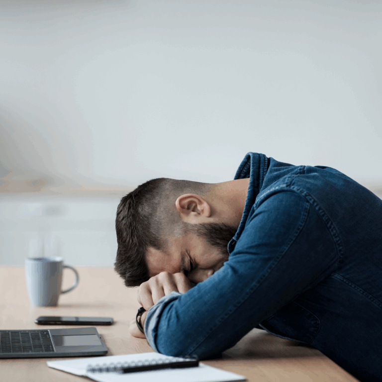 profile view of man with head down on arms, on desk, looking tired