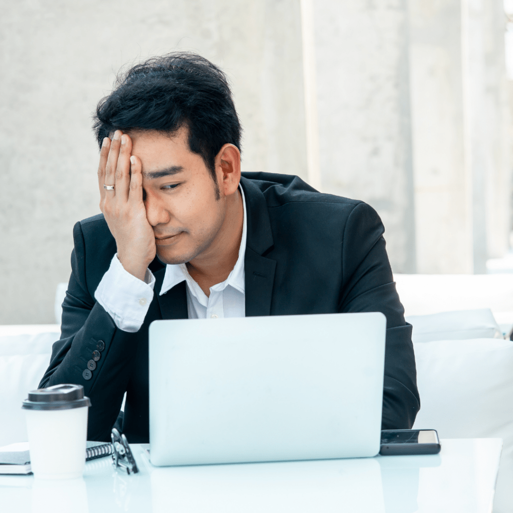 man with hand on face, stressed, looking at laptop at work