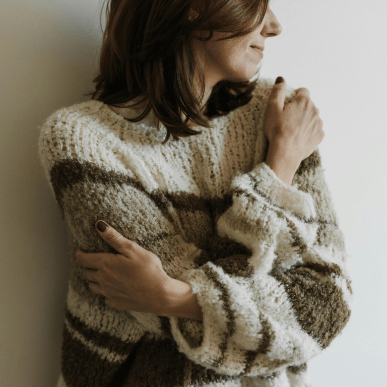 woman looking off to side hugging herself