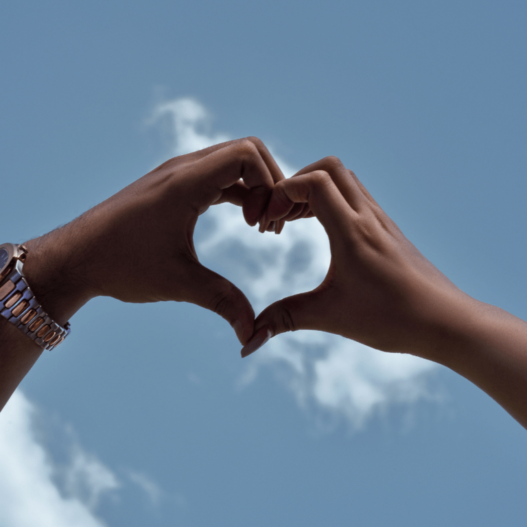 hands forming heart sky in background
