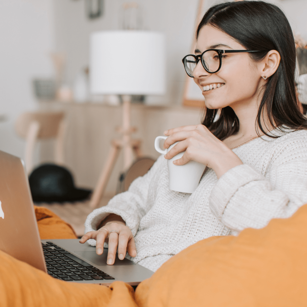 woman holding cup of coffee, on her laptop at home